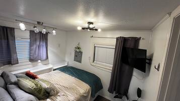 A bedroom with a bed, a window with curtains, a ceiling fan, and a mounted television.