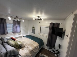 A bedroom with a bed, a window with curtains, a ceiling fan, and a mounted television. - Lovely 1-bedroom mobile home with AC in peaceful Cherokee (Cherokee)