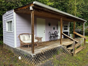 A wooden porch with a covered seating area, a grill, and a door leading to the interior. - Lovely 1-bedroom mobile home with AC in peaceful Cherokee (Cherokee)