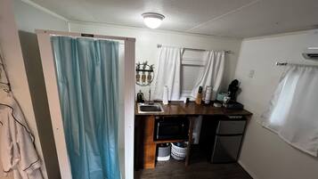 A compact kitchen with a sink, a small refrigerator, and a window with curtains.