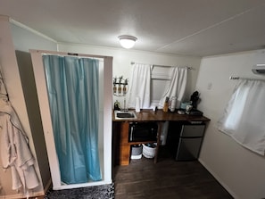 A compact kitchen with a sink, a small refrigerator, and a window with curtains.