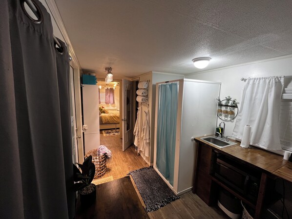 A narrow hallway leading to a bedroom with a bed, a small kitchenette, and a bathroom with a shower curtain.