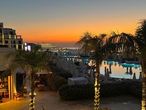 Zona de piscina en un resort con sombrillas, sillas de descanso y vistas al atardecer.
