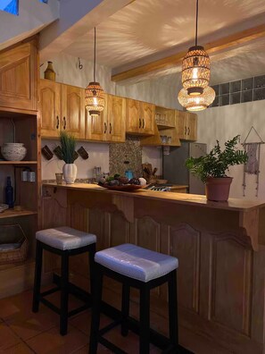 A kitchen with wooden cabinets, a bar area with stools, and pendant lighting. - Casa Bentley: 360° rooftop terrace + lush garden (San Pedro La Laguna)