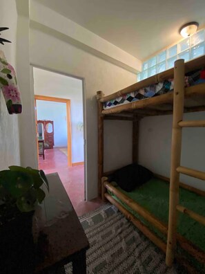 A bunk bed with a green mattress, a wooden table with a plant, and a patterned rug. - Casa Bentley: 360° rooftop terrace + lush garden (San Pedro La Laguna)