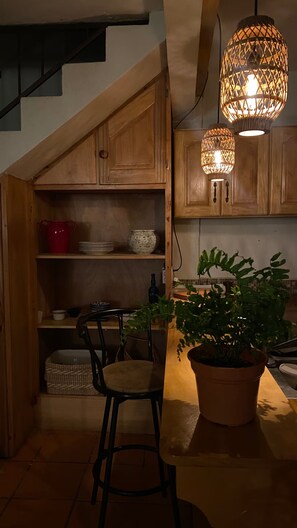 A kitchen with wooden cabinets, a red pot, a bowl, a potted plant, and two hanging lights. - Casa Bentley: 360° rooftop terrace + lush garden (San Pedro La Laguna)