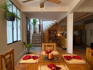 A dining area with a table set for four, a staircase leading to a kitchen, and a ceiling fan. - Casa Bentley: 360° rooftop terrace + lush garden (San Pedro La Laguna)