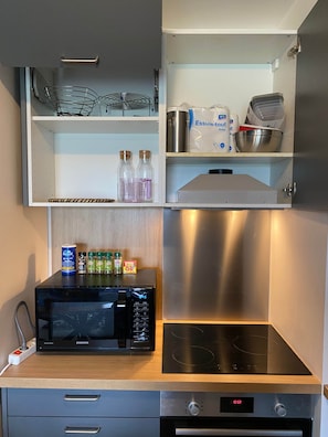 Een keuken met een magnetron, fornuis en diverse keukenbenodigdheden op planken.