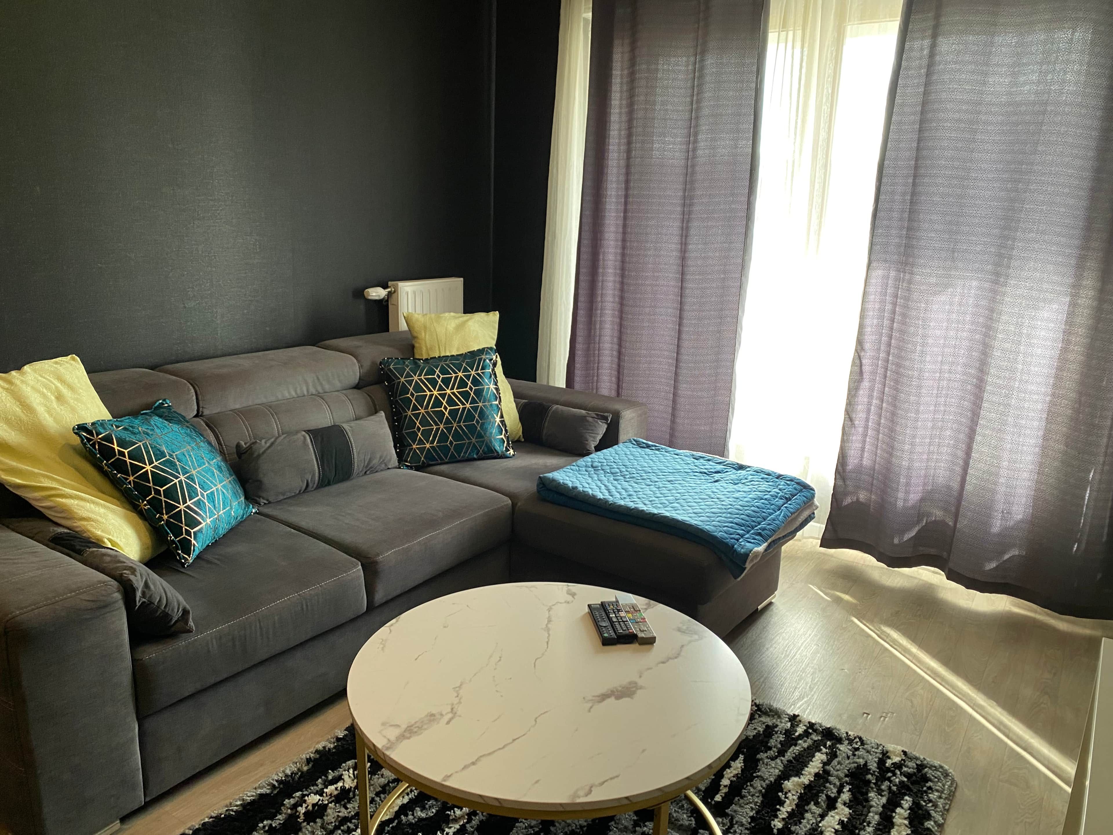 Een woonkamer met een grijze bank, een ronde salontafel en een afstandsbediening erop.