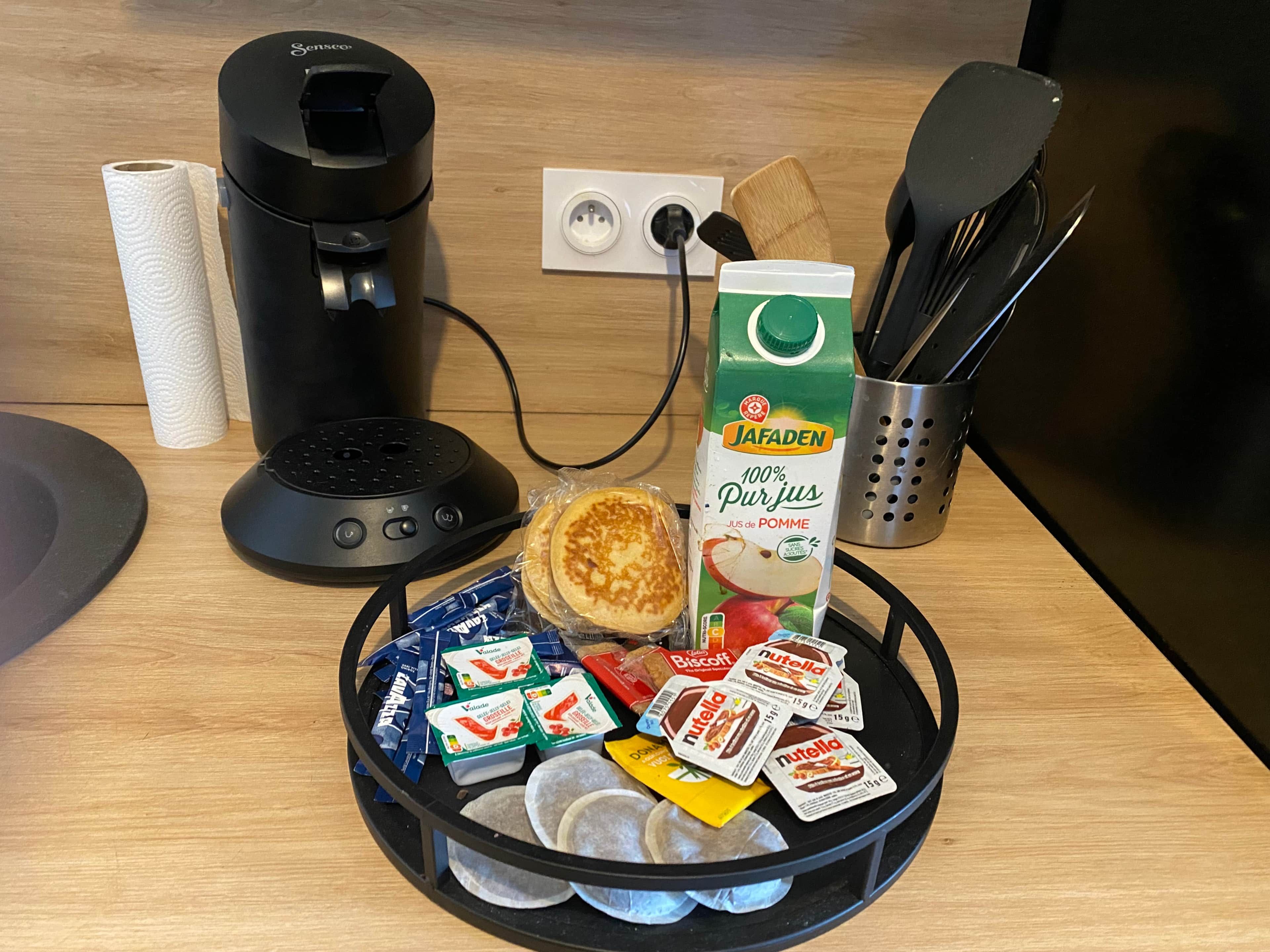 Een keukentrap met een koffiezetapparaat, een pak Jafaden-sap, een spatel, een messenblok en een schaal met etenswaren, waaronder Nutella en koekjes.