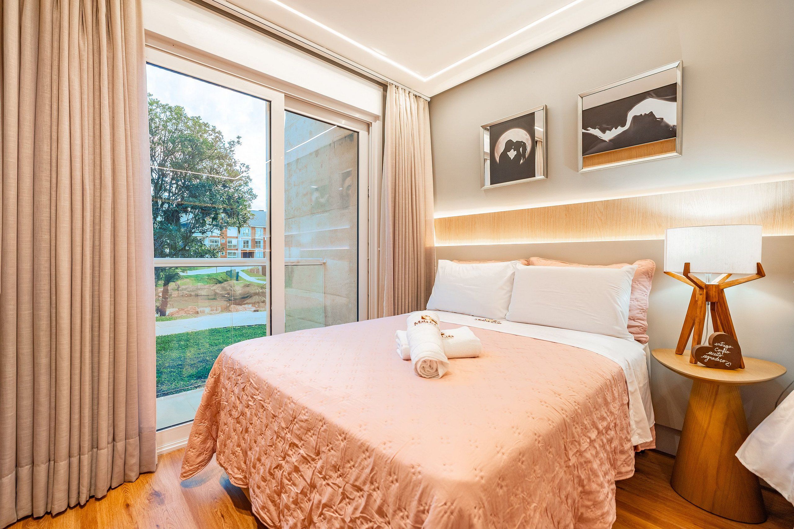 A hotel room with a bed, a nightstand, a lamp, and two framed pictures on the wall.