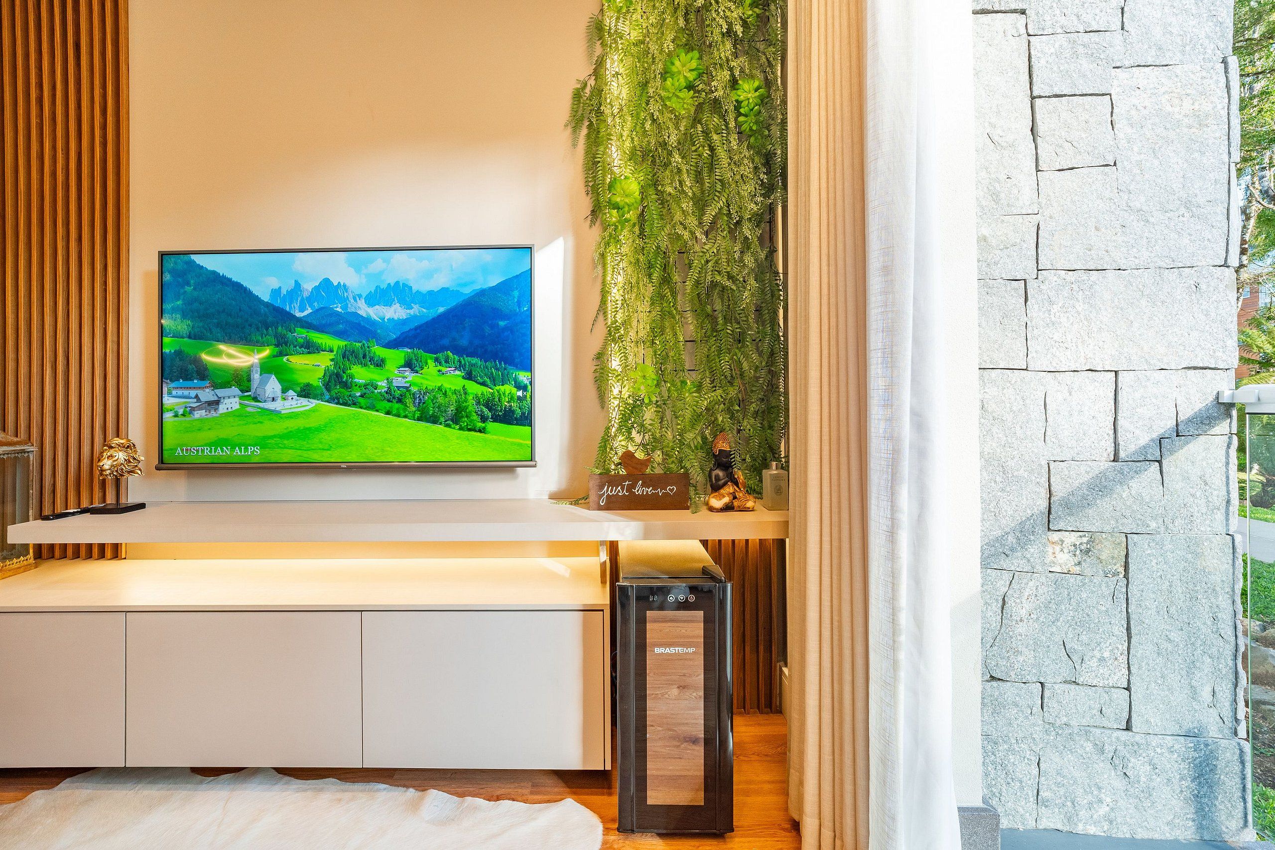 Ein modernes Wohnzimmer mit einem an der Wand befestigten Flachbildfernseher, einer kleinen Statue und einer Zierpflanze.
