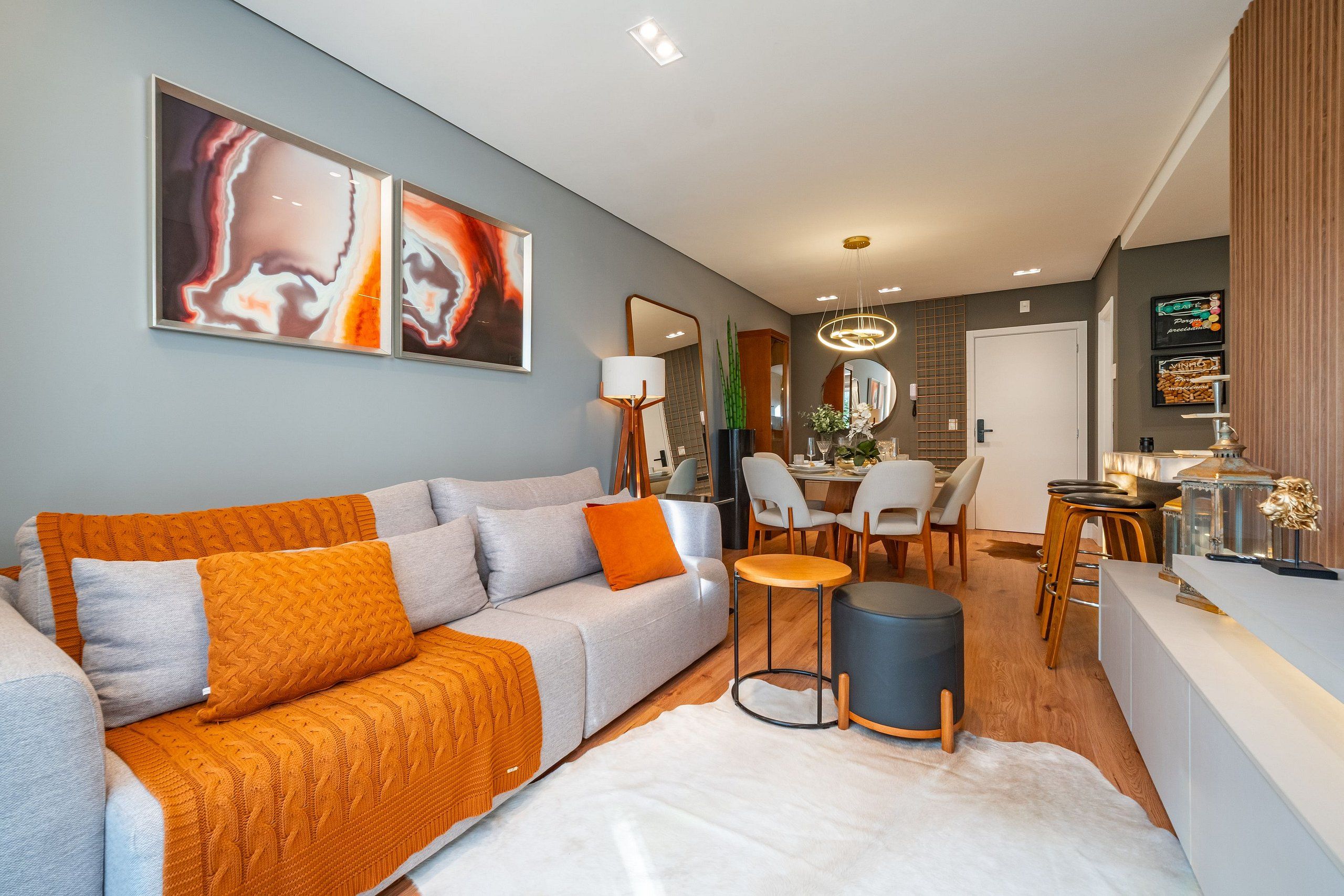 A modern living room with a grey sofa, orange cushions, a coffee table, and a dining area with chairs and a table.