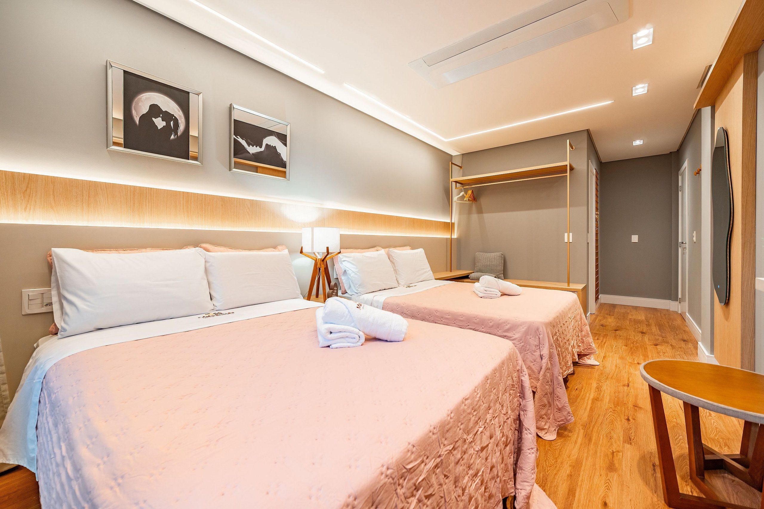 A hotel room with two beds, a bedside table, a chair, and a wall-mounted shelf.