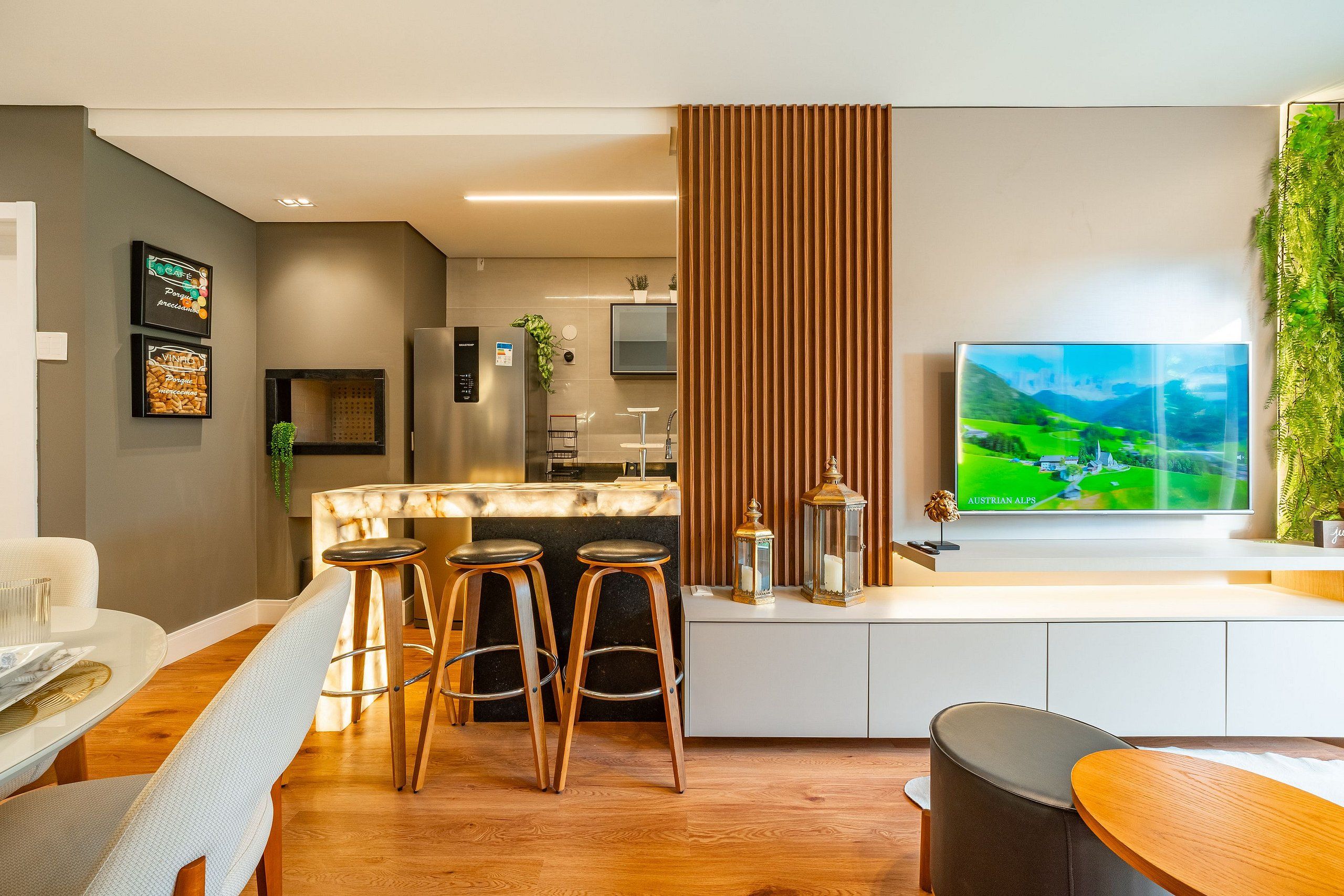 Una cocina moderna con barra, una zona de comedor con mesa redonda y un televisor grande mostrando un paisaje.