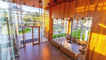 A modern lobby with glass doors, a herringbone floor, and a seating area with sofas.