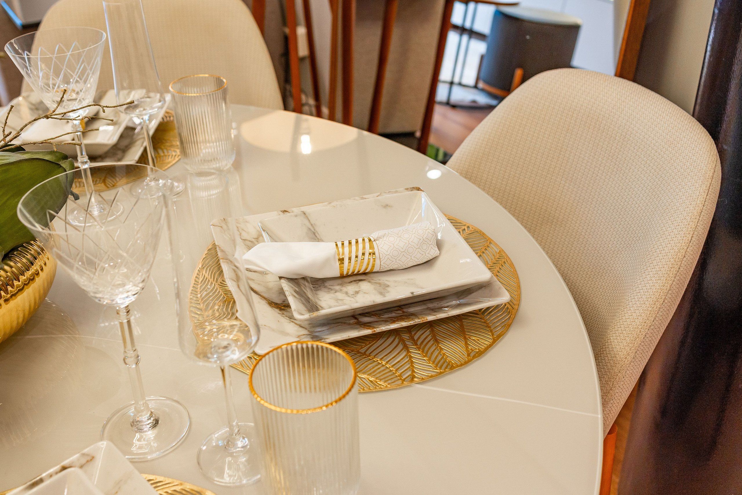 A dining table set with clear glassware, a folded napkin, and a decorative leaf-patterned placemat.