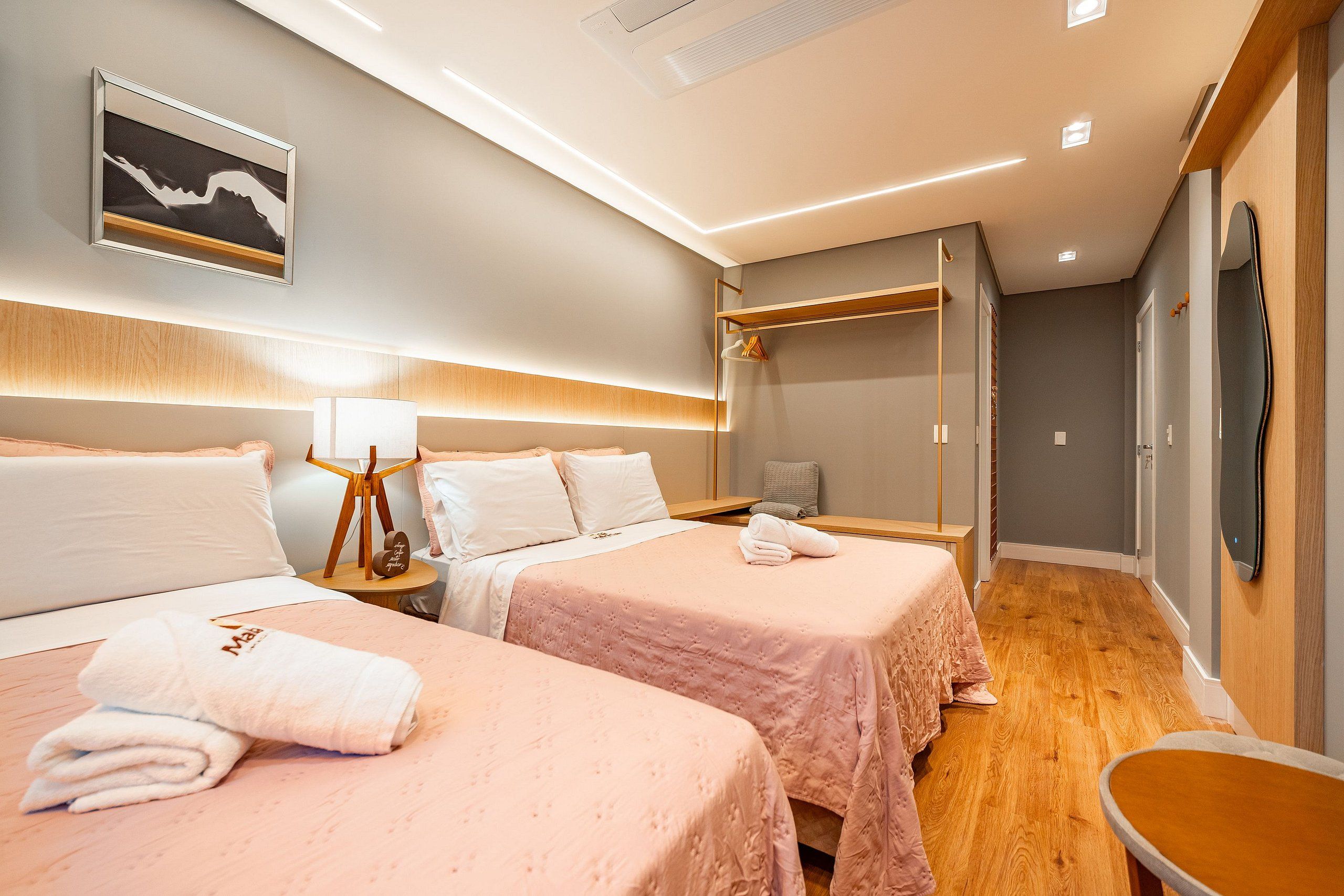 A hotel room with two beds, a bedside table with a lamp, a mirror, and a wardrobe.