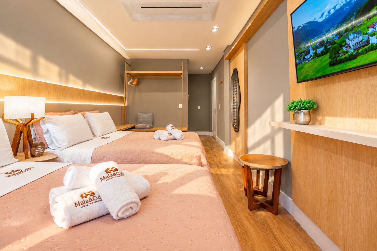 A hotel room with two beds, a TV on the wall, a small table, and a potted plant.