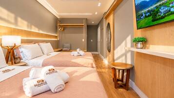 A hotel room with two beds, a TV on the wall, a small table, and a potted plant.