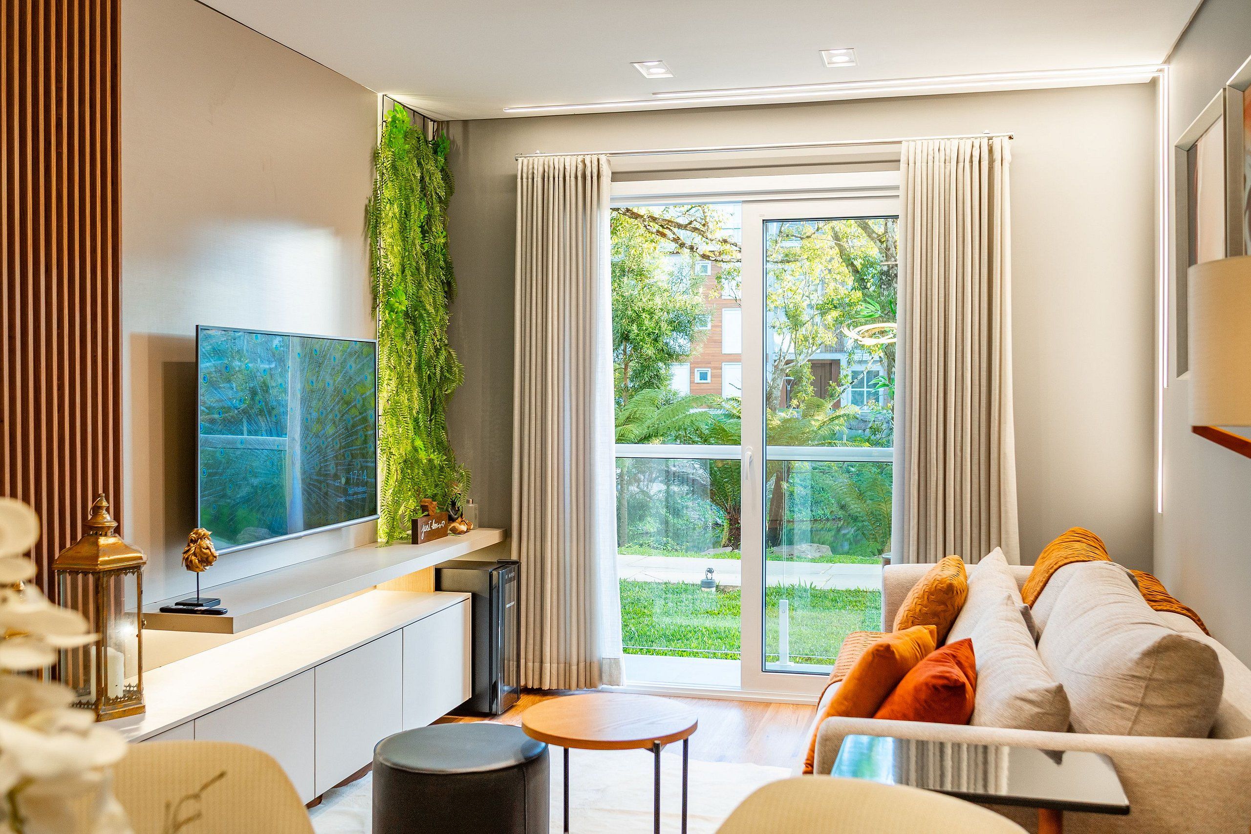 A modern living room with a sofa, a coffee table, a TV, and a large window with curtains.