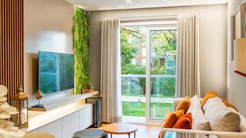 A modern living room with a sofa, a coffee table, a TV, and a large window with curtains.