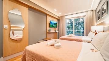 A hotel room with two beds, a TV, a window with a view, and a mirror on the wall.
