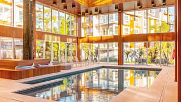 Un área de piscina interior moderna con techo de vidrio, paneles de madera y asientos junto a la piscina.