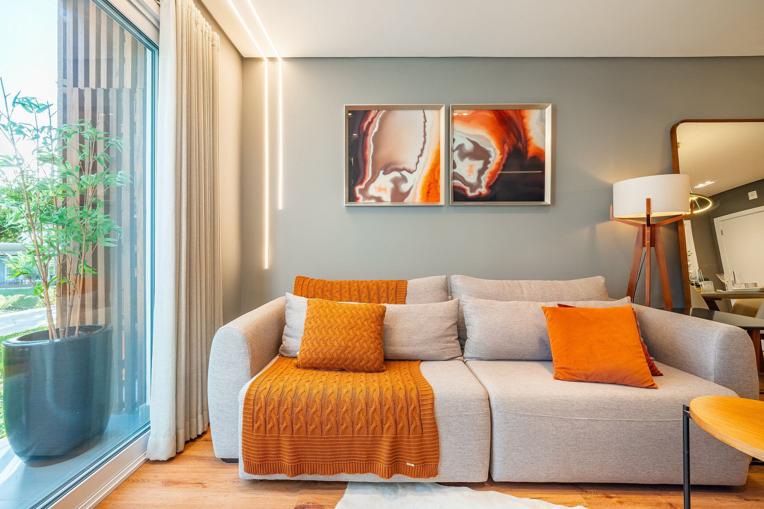 Ein modernes Wohnzimmer mit einer Couch, Kissen, einem großen Fenster und Kunstwerken an der Wand.