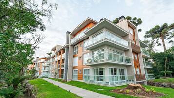 Un edificio residencial de varios pisos con balcones, un sendero pavimentado y zonas verdes circundantes.