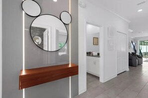 A modern interior with a wooden console table, a wall-mounted mirror, and a kitchen area visible through an open door. - 5BR house with private pool in Storey Lake (Kissimmee)