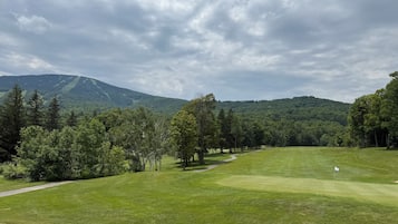 A golf course with a path leading to the tee area, surrounded by trees and a mountain in the background.