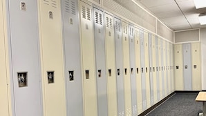 A row of lockers with numbers on them, a carpeted floor, and a bench.