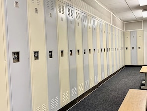 A row of lockers with numbers on them, a carpeted floor, and a bench.