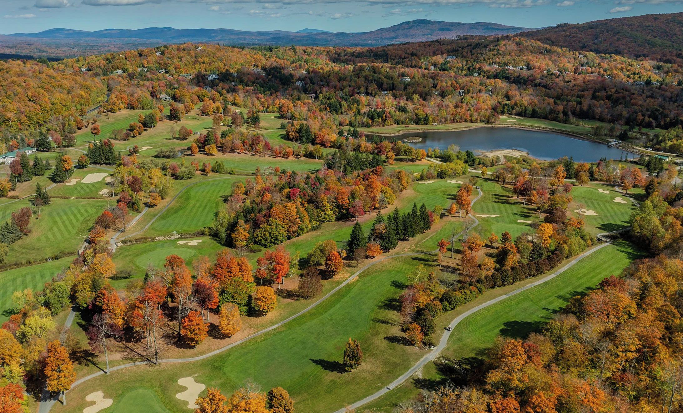 A golf course with multiple fairways, sand traps, and a lake.