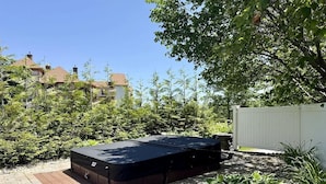A hot tub in a garden with a paved area, surrounded by greenery and a white fence.