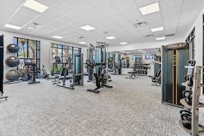 Ein modernes Fitnessstudio mit unterschiedlichen Trainingsgeräten, großen Fenstern und einem Teppichboden.