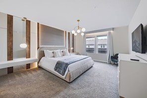 Ein modernes Schlafzimmer mit einem großen Bett, Nachttischen, einem Schreibtisch und einem Fernseher.