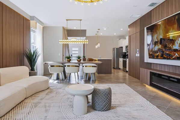 A modern living room with a sofa, dining area, kitchen, and a TV displaying a fireplace. - 7BR house with private pool in clermont (Clermont)