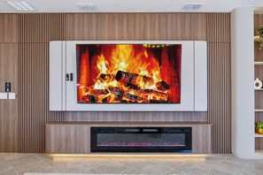 A modern living room with a large flat-screen TV mounted on a wooden wall, a fireplace below, and a built-in entertainment system. - 7BR house with private pool in clermont (Clermont)