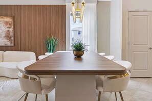 A modern dining room with a wooden table, white chairs, a chandelier, and a potted plant. - 7BR house with private pool in clermont (Clermont)