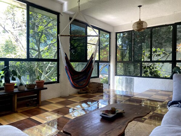 A room with large windows, a hammock, a wooden table, and potted plants. - Rockhouse - Steps to Water - Garden - F Optic (San Pedro La Laguna)
