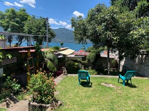 A backyard with a view of a lake and mountains, two blue chairs, and a small garden with flowers. - Rockhouse - Steps to Water - Garden - F Optic (San Pedro La Laguna)