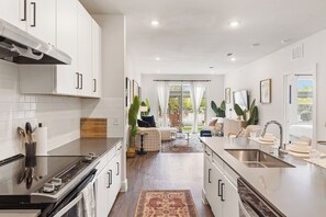 A modern kitchen with white cabinets, a stainless steel sink, and a dining area with a sofa and table. - Luxury 1BR 1BA Apartment (Austin)