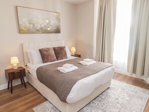 A hotel room with a large bed, two bedside tables with lamps, a decorative wall piece, and a view of the outdoors. - Flat 1 (Tenby)