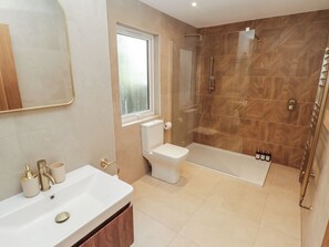 Une salle de bain avec un lavabo blanc, des robinetteries dorées, des toilettes, une douche et un miroir.