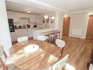 A modern kitchen with white cabinets, a central island, and pendant lighting. - Flat 1 (Tenby)