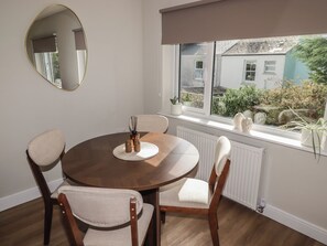 A dining area with a round table, four chairs, a mirror, and a window with a view of a garden and buildings. - Flat 2 (Tenby)