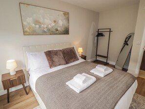 A neatly made bed with a patterned bedspread, a bedside lamp, and a wall-mounted abstract painting. - Flat 2 (Tenby)