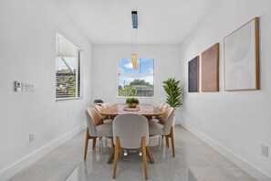 A modern dining room with a round table, six chairs, a potted plant, and artwork on the walls. - Brand-New Cape Coral Oasis 4BR/3BA + Heated Saltwater Pool + Waterfront (Cape Coral)